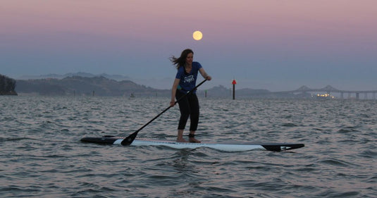 A Stand up paddleboarder glides under the moon on San Francisco Bay