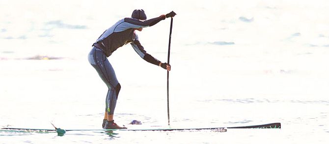 A stand up paddler well dressed for colder weather